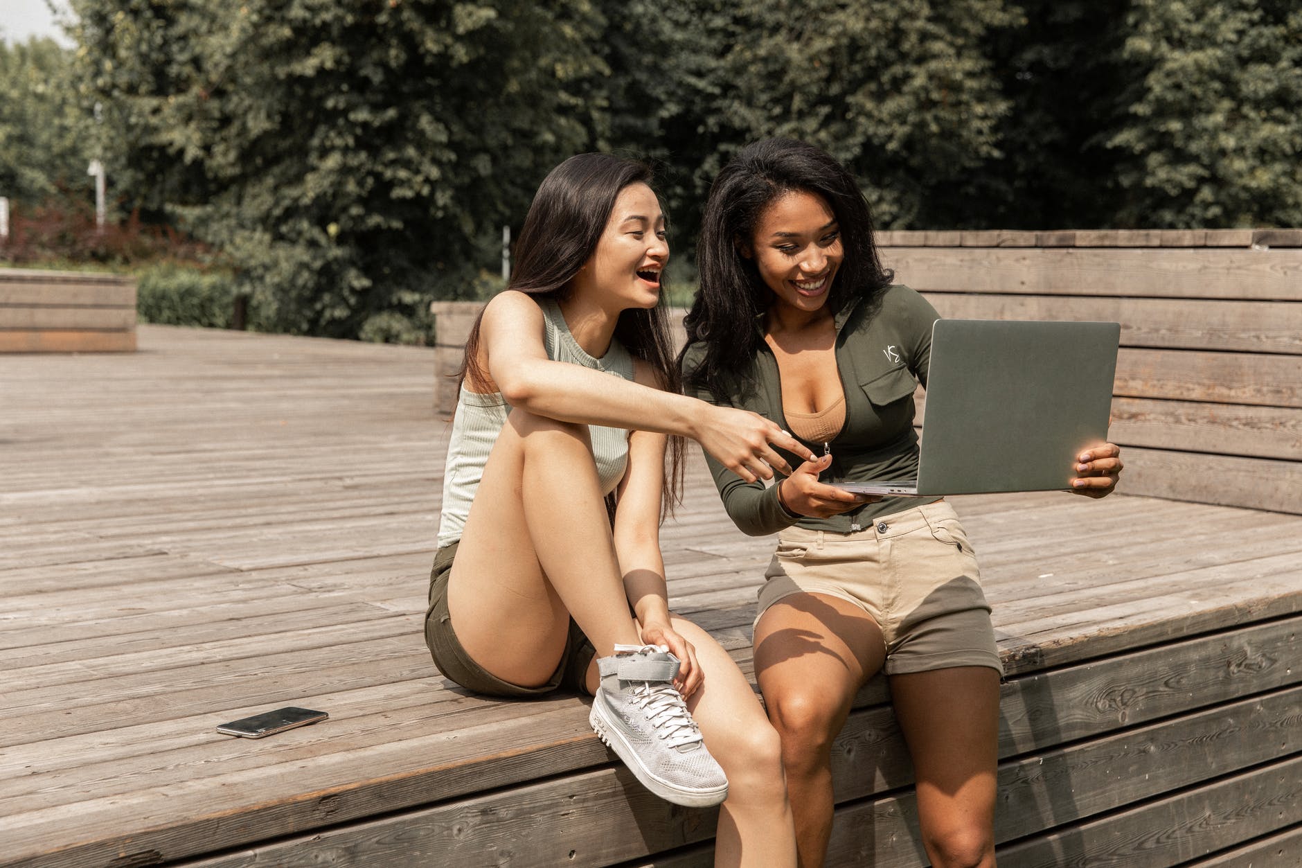 cheerful young multiethnic women sharing laptop and laughing in park